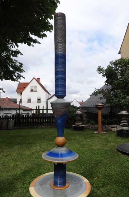 Moderner Gartenbrunnen aus winterfester Keramik mit gerillter Säule und Lichtreflexen über zwei farbige Kegel, sehr leise