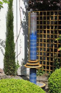Moderner Gartenbrunnen aus winterfester Keramik mit gerillter Säule und kaskadenförmiges Abtropfen über Teller, dezente Akustik